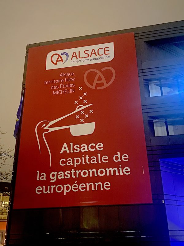 Une affiche rouge avec une cigogne dessinée en blanc avec écrit: Alsace Capitale de la gastronomie européenne