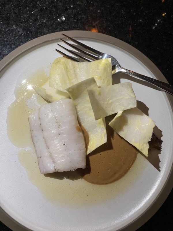 dans une assiette beige, un morceau de filert de poisson blanc des endives coupées et une sauce brune