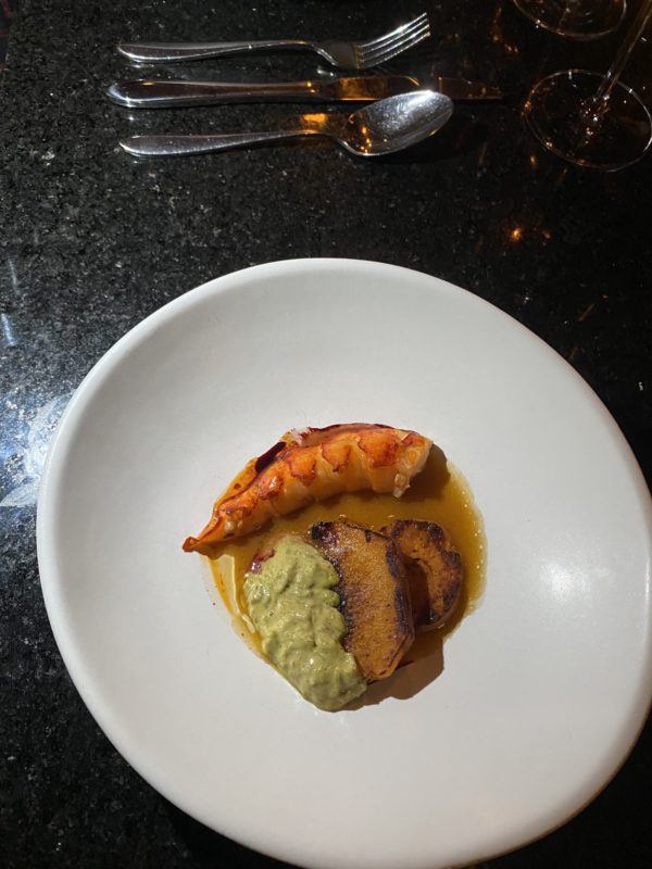 une assiette blanche au milieu une sauce brune, une queue de homard et un légume vert