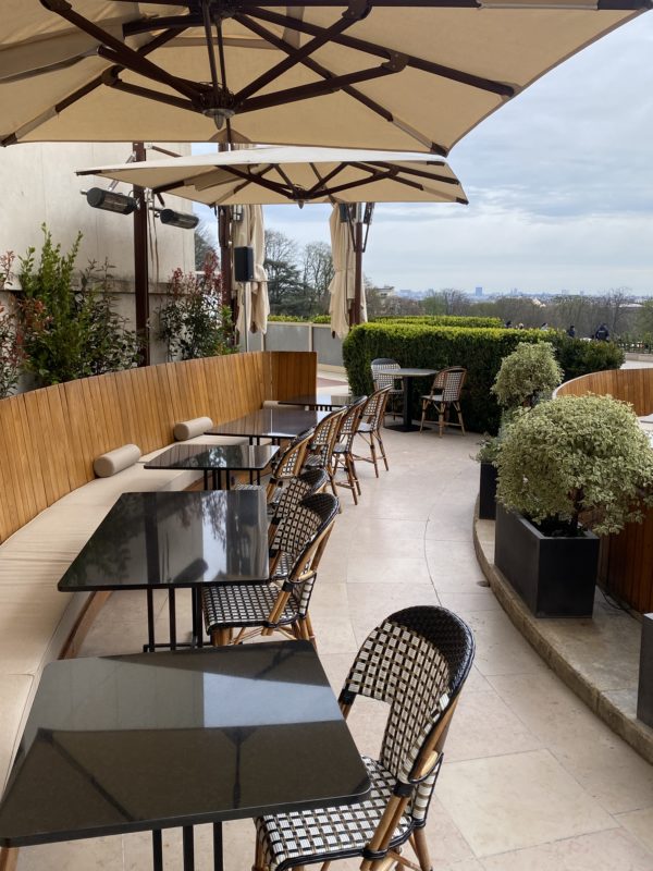 Tables en terrasse avec parasols beige et plantes topiaires