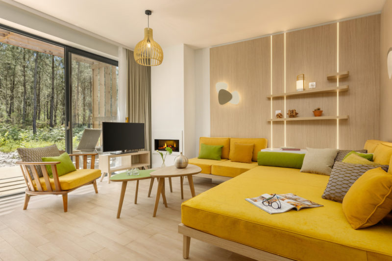 Un intérieur de maison avec vue sur le jardin Mobilier de bois  et canapé jaune et vert 