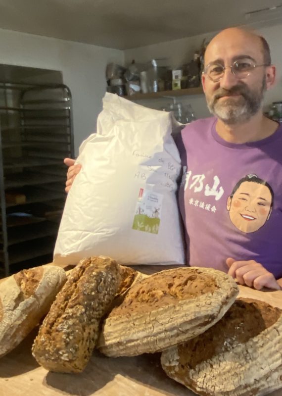 le boulanger dans son fournil tenant un sac de farine et montrant ses pains 